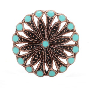 May include: A round, decorative metal piece with a floral design. The piece features a copper-colored frame with a black filigree pattern and turquoise-colored accents. The design is symmetrical and detailed, with a central turquoise dot.
