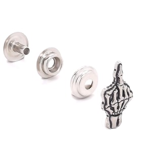 May include: Silver metal snap fasteners with a silver metal skeleton middle finger charm.