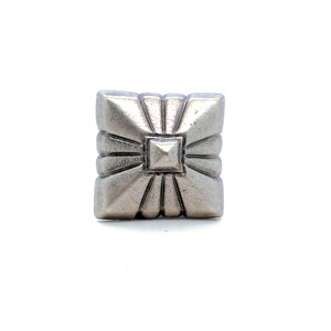 May include: A square silver-toned metal button featuring a raised central pyramid shape surrounded by radiating embossed lines that extend toward the four edges, creating a geometric sunburst pattern with a smooth, polished metallic finish.