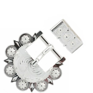 May include: Silver belt buckle with a decorative design featuring a crescent moon and a circle pattern. The buckle is designed to be used with a belt strap.