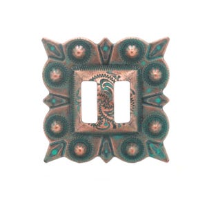 May include: A decorative, square light switch cover with a copper-colored finish and turquoise accents. The cover features an ornate, embossed design with two rectangular openings for the switches.
