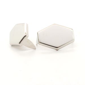 May include: Two silver-colored metal studs with a geometric design. One stud is a rectangular shape with a pointed post, and the other is a hexagon shape. The studs are on a white background.