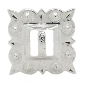 May include: Silver-toned metal buckle with a square shape and a decorative design. The buckle has a center opening with two slots for a strap.