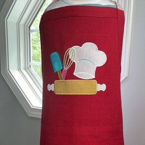 Customer review picture embroidered on an apron.Embroidered rolling pin with spatula, whisk and chef hat.  In the background is a picture of the same design that show what the design would look like the name Cassandra added.