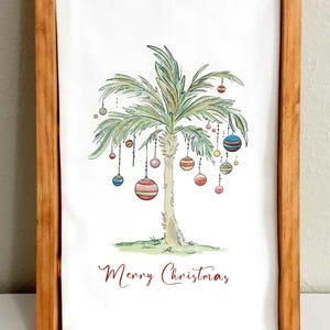 May include: A white rectangular tea towel featuring a watercolor illustration of a palm tree decorated with colorful hanging Christmas ornaments. The text Merry Christmas is printed in red below the tree, with IdleTymeCreations.etsy.com at the bottom.