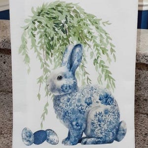 May include: A white rectangular kitchen towel featuring a watercolour illustration of a rabbit with a blue and white floral pattern. Above the rabbit hangs green willow foliage, and three blue speckled eggs sit at its feet. IdleTymeCreations.etsy.com