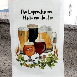 May include: White kitchen towel with a green shamrock and the text "The Leprechauns Made me do it". The towel features a watercolor illustration of four glasses of beer with a green shamrock and a leprechaun.