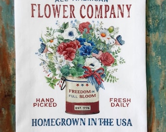 May include: White kitchen towel with a floral design. The towel features a bouquet of red, white, and blue flowers in a metal bucket. Text includes "All-American Flower Company", "Freedom in Full Bloom", and "Homegrown in the USA".