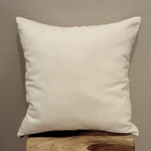 May include: A plain white pillow with a smooth, even surface. The pillow is sitting on a wooden surface.