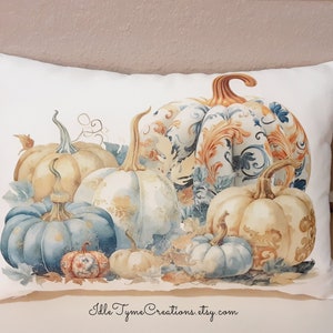 May include: A white pillow with a watercolor design of blue, white, and orange pumpkins. The pumpkins are arranged in a cluster and have a decorative, ornate pattern. The pillow has the text "Idle Tyme Creations.etsy.com" at the bottom.
