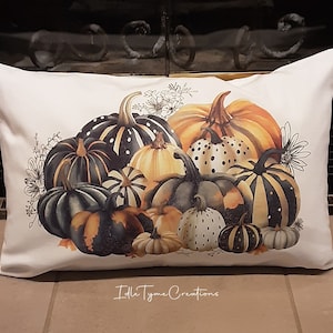 May include: A white pillow with a colorful illustration of a group of pumpkins in various shades of orange, black, and white. The pumpkins are arranged in a pile and have different patterns, including stripes, dots, and swirls. The pillow has the text "Idle Thyme Creations" printed on the bottom.