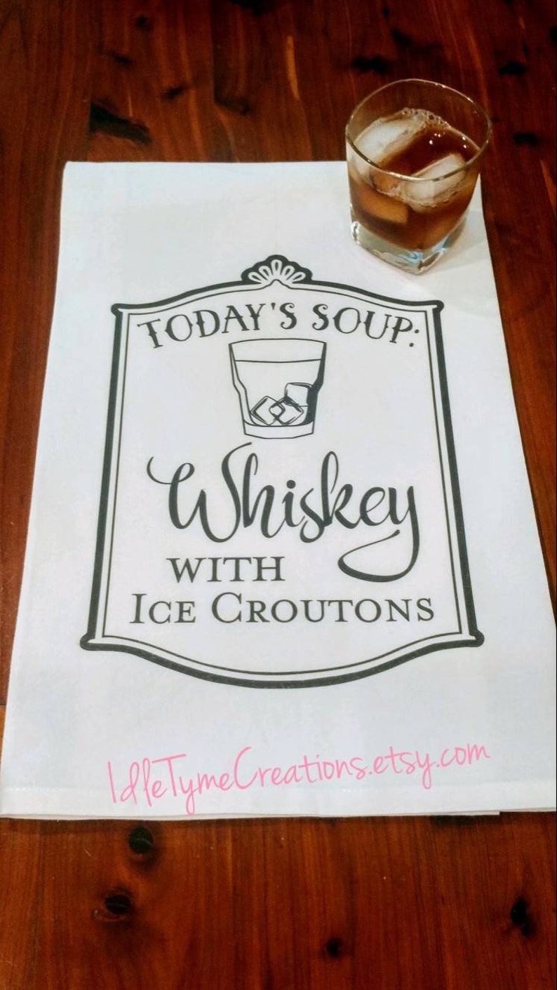 May include: White kitchen towel with black text that reads "Today's Soup: Whiskey with Ice Croutons". A glass of whiskey with ice is pictured above the text.