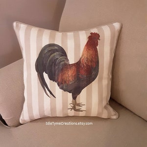 May include: A decorative throw pillow with a white and brown striped background featuring a colorful rooster illustration. The pillow has a white border and the text "idleTymeCreations.etsy.com" is printed on the bottom.