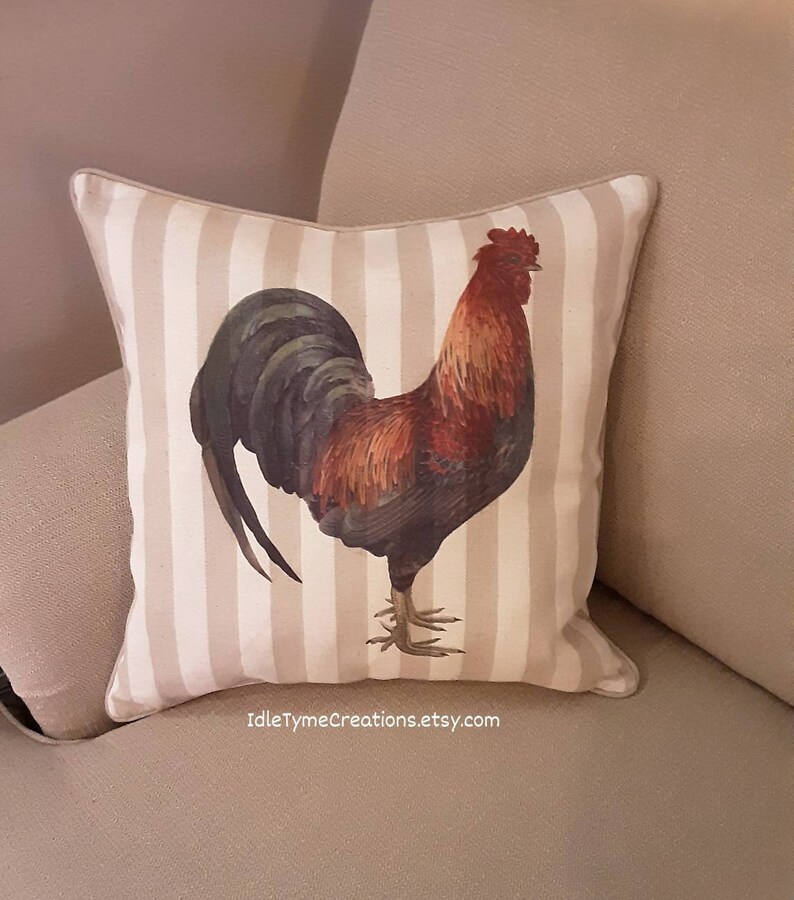 May include: A decorative throw pillow with a white and brown striped background featuring a colorful rooster illustration. The pillow has a white border and the text "idleTymeCreations.etsy.com" is printed on the bottom.