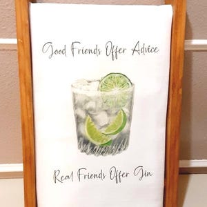 May include: A white kitchen towel featuring a watercolor illustration of a glass filled with ice and lime slices. The text reads Good Friends Offer Advice, Real Friends Offer Gin. The towel is draped over a vertical wooden frame stand.