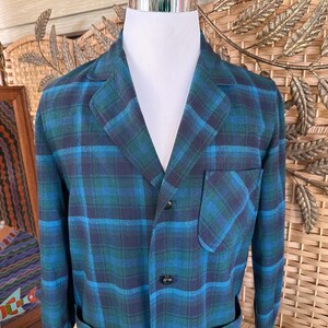 Puede incluir: Una blazer a cuadros azul y verde con solapas, un bolsillo en el pecho y dos bolsillos delanteros. La blazer est&aacute; abrochada y se muestra en un maniqu&iacute; blanco. El patr&oacute;n de cuadros es una mezcla de azul oscuro, verde azulado y verde.