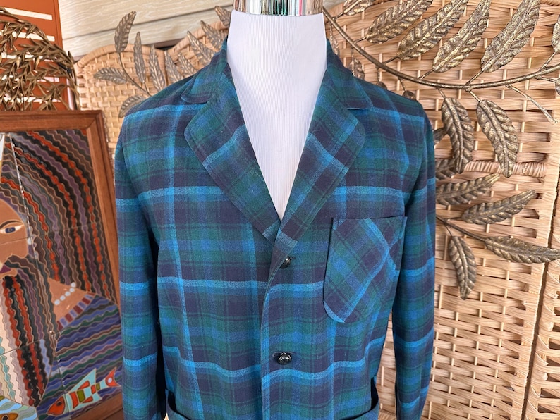 Puede incluir: Una blazer a cuadros azul y verde con solapas, un bolsillo en el pecho y dos bolsillos delanteros. La blazer est&aacute; abrochada y se muestra en un maniqu&iacute; blanco. El patr&oacute;n de cuadros es una mezcla de azul oscuro, verde azulado y verde.