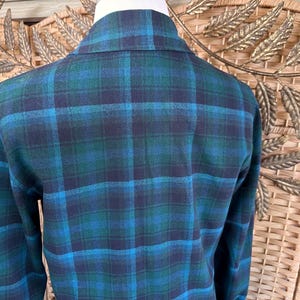 Puede incluir: Un blazer a cuadros azul y verde. El blazer tiene un cuello cl&aacute;sico y mangas largas. El patr&oacute;n de cuadros es una mezcla de azul oscuro, verde azulado y azul claro. La tela parece ser un material suave y tejido.