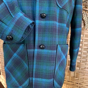 Puede incluir: Chaqueta vintage a cuadros en tonos turquesa, azul marino y verde. La chaqueta presenta un patr&oacute;n de cuadros cl&aacute;sico, botones negros y dos bolsillos delanteros. El pu&ntilde;o de la manga es visible y la chaqueta parece estar hecha de una mezcla de lana.