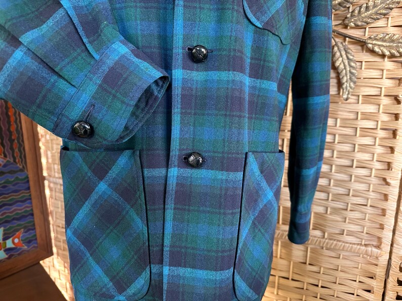 Puede incluir: Chaqueta vintage a cuadros en tonos turquesa, azul marino y verde. La chaqueta presenta un patr&oacute;n de cuadros cl&aacute;sico, botones negros y dos bolsillos delanteros. El pu&ntilde;o de la manga es visible y la chaqueta parece estar hecha de una mezcla de lana.