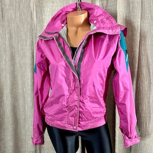 May include: A pink hooded jacket with teal accents and a zipper closure. The jacket has a fleece lining and a drawstring hood.