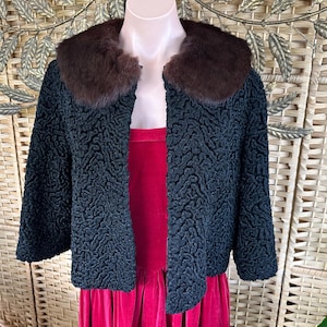 May include: A dark teal jacket with a textured pattern and a brown fur collar. The jacket is open in the front, revealing a red dress underneath. The jacket has three-quarter length sleeves.