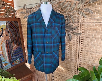 May include: A vintage plaid blazer in shades of teal and blue, displayed on a mannequin. The jacket features a classic notched collar, three buttons, and two front pockets. The plaid pattern is a bold, eye-catching design.