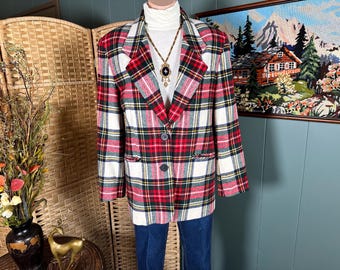 May include: A long-sleeve blazer featuring a red, white, green, and black plaid pattern with notched lapels and two dark buttons. The garment is worn over a white turtleneck sweater and includes a long necklace with a dark pendant.