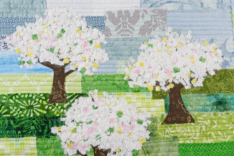 May include: A quilt depicting three trees with white, pink, and yellow blossoms against a blue and green background. The trees are made of fabric scraps and are sewn together to create a patchwork effect.