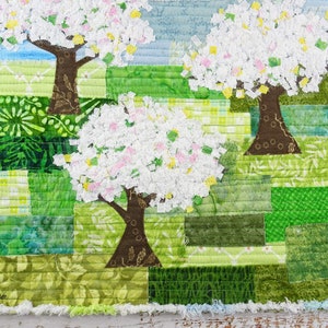 May include: A patchwork quilt featuring three stylized trees with white blossoms against a green and blue background.
