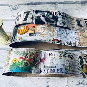 May include: Three decorative paper strips with vintage designs. One strip features a hot air balloon and the word "TRAVEL". Another strip has floral and botanical illustrations with the text "NATURE". A map-covered spool is in the background.