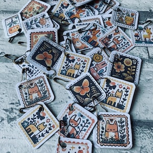 May include: A collection of colourful square-shaped pins featuring various animal and floral illustrations. The pins are attached to safety pins, making them ideal for adding a touch of whimsy to clothing, bags, or other accessories.