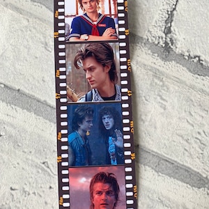 May include: A film strip bookmark with four images of a young man with brown hair. The images are in black and white and color. The bookmark is made of paper and has a black background with white film strip markings.