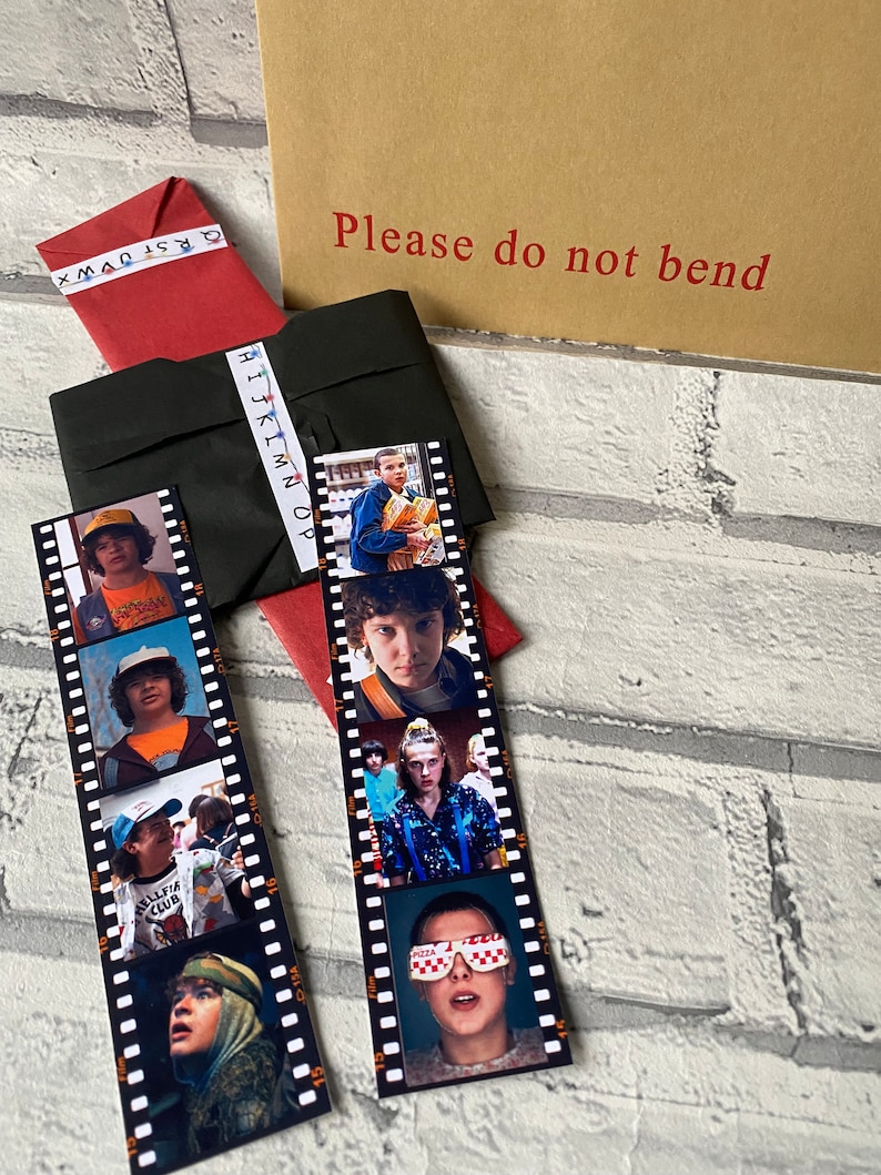 May include: Two black and white film strip bookmarks featuring characters from the show Stranger Things. The bookmarks have images of Eleven, Mike, Dustin, and Lucas.