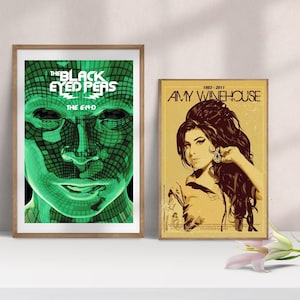 May include: Two framed posters on a white surface. The left poster features a green face with the text "THE BLACK EYED PEAS THE E-N-D". The right poster is a portrait of Amy Winehouse with the text "1983-2011 AMY WINEHOUSE".