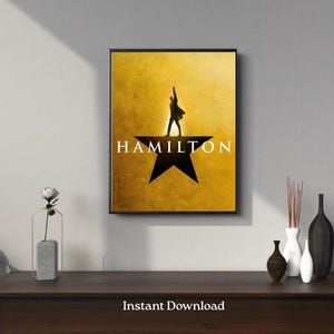 May include: A framed poster with the word "HAMILTON" in white letters over a black star. The poster features a silhouette of a person with an arm raised against a gold background. The words "Instant Download" are at the bottom.