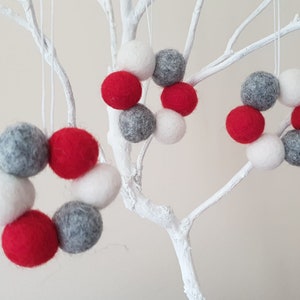 May include: Three felt Christmas ornaments in the shape of wreaths. The wreaths are made of red, white, and gray felt balls.