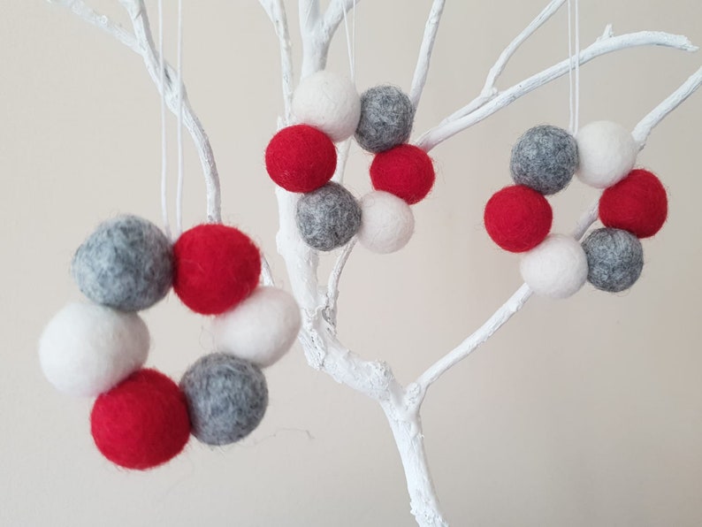 May include: Three felt Christmas ornaments in the shape of wreaths. The wreaths are made of red, white, and gray felt balls.