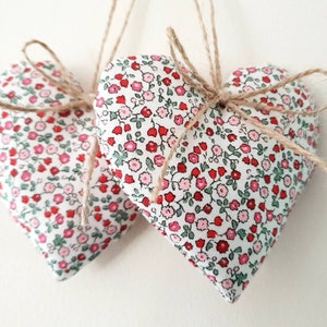 May include: Two white fabric hearts with a red and pink floral pattern, tied together with twine.