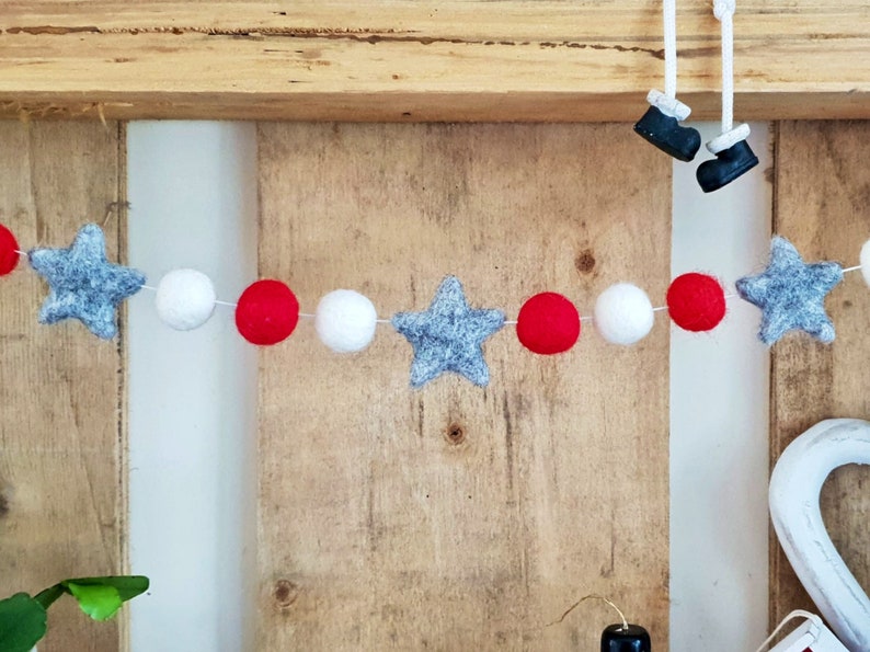 May include: A festive garland with red, white, and gray felt balls and stars. The garland is strung on white thread and is perfect for decorating for the holidays.