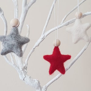 May include: Three felt star ornaments hanging from a white branch. The stars are gray, white, and red.