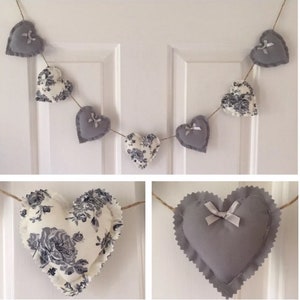 May include: A garland of grey and white fabric hearts with floral patterns and white satin bows. The garland is strung on twine and is perfect for a nursery or bedroom.