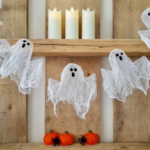 Peut inclure: Une guirlande de fant&ocirc;mes en gaze blanche suspendue &agrave; une &eacute;tag&egrave;re en bois avec trois bougies piliers blanches sur l'&eacute;tag&egrave;re. Il y a deux citrouilles en feutre orange avec des araign&eacute;es noires sur l'&eacute;tag&egrave;re du bas.