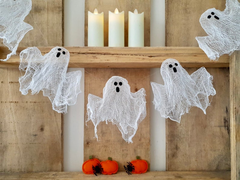 Peut inclure: Une guirlande de fant&ocirc;mes en gaze blanche suspendue &agrave; une &eacute;tag&egrave;re en bois avec trois bougies piliers blanches sur l'&eacute;tag&egrave;re. Il y a deux citrouilles en feutre orange avec des araign&eacute;es noires sur l'&eacute;tag&egrave;re du bas.