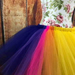 May include: A rainbow tulle skirt with layers of blue, purple, pink, orange, and yellow tulle. The skirt is gathered at the waist and has a stretchy waistband.