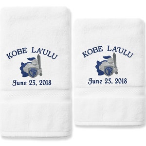 May include: Two white bath towels with embroidered blue text and a knight design. The text reads "KOBE LA'ULU June 23, 2018".