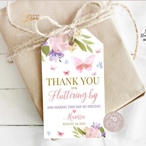 May include: A gift tag with a floral butterfly design. The tag reads "THANK YOU FOR Fluttering by" with the name "Marissa" and the date "August 18, 2025". The tag is tied to a wrapped gift with twine.