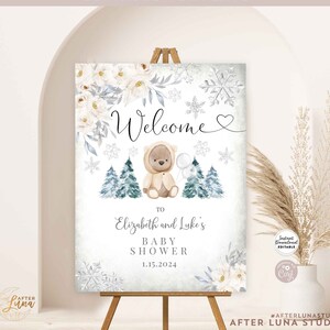May include: A printable welcome sign for a baby shower with a winter theme. The sign features a white background with snowflakes, a watercolour floral design, and a cute cartoon bear wearing a hat and holding a balloon. The text on the sign reads "Welcome to Elizabeth and Luke's Baby Shower 1.15.2024".