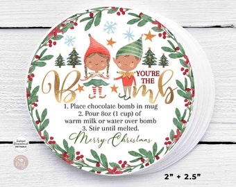 Könnte beinhalten: Rundes Weihnachtsetikett mit dem Text "You're the Bomb" in goldener Schrift. Das Etikett zeigt Illustrationen von Elfen, Weihnachtsbäumen und Schneeflocken, umgeben von einem grünen und roten Kranz. Gebrauchsanweisungen sind enthalten. Das Etikett misst 5,08 cm x 6,35 cm.