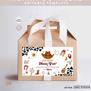 Puede incluir: Una caja de regalo marrón con una cinta blanca y una etiqueta blanca con un sombrero de vaquero, estrellas y el texto "Yee-Haw! Thanks, Y'all!" para una fiesta de cumpleaños.